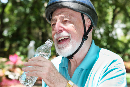 Active senior man wearing a bicycle helmet stops to drink bottled water.